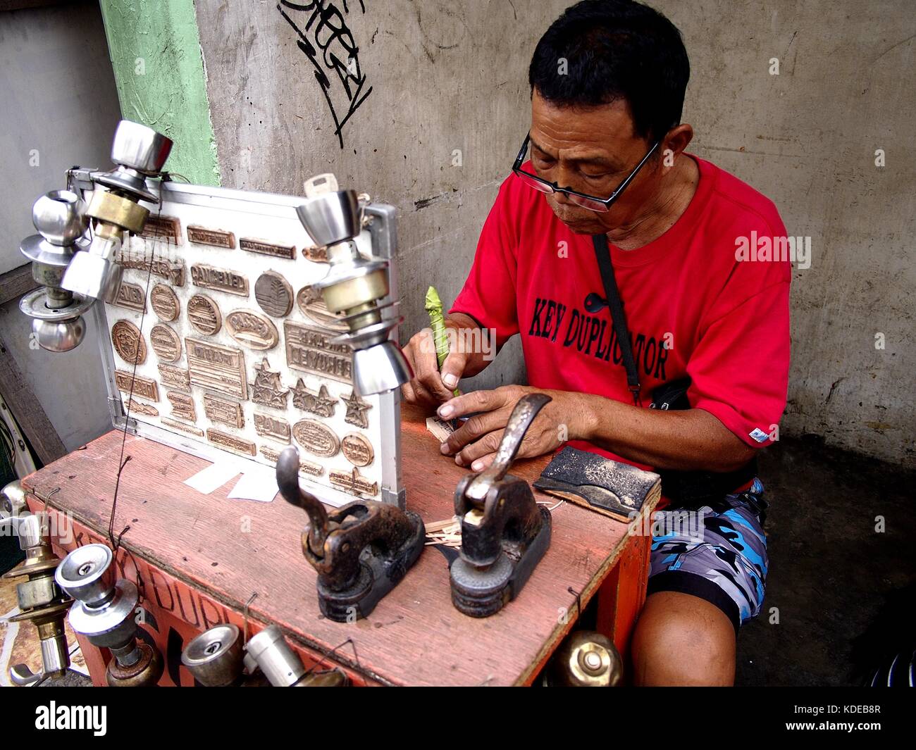 Antipolo CITY, PHILIPPINES - 12 OCTOBRE 2017 : un serrurier et fabricant de timbres crée un bloc de timbres pour un client à son étal de fortune près d'un trottoir. Banque D'Images