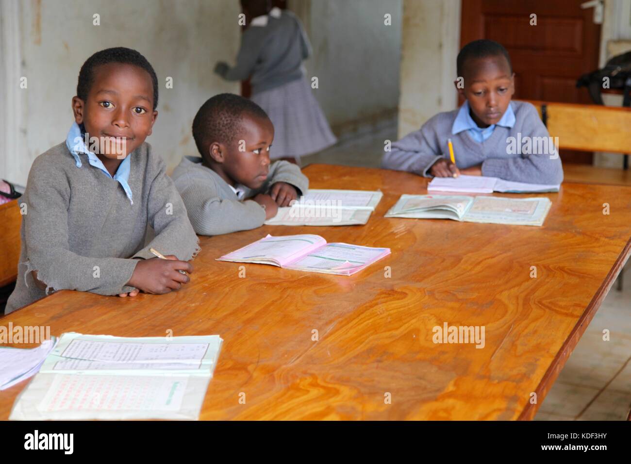 Trois garçons de l'école africaine le port de l'uniforme s'asseoir à un bureau étudiant, un garçon regarde en souriant de l'appareil photo Banque D'Images