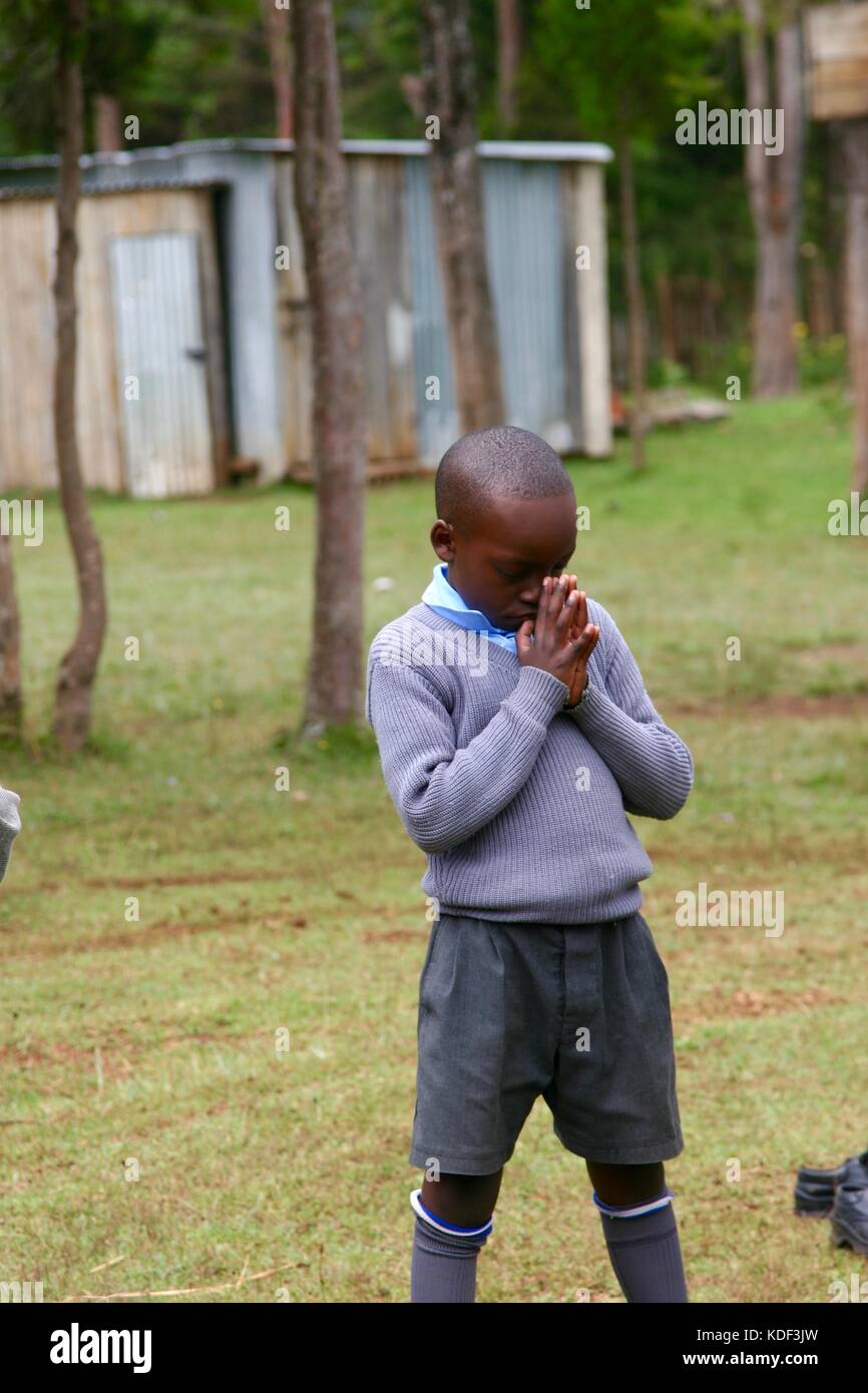 Jeune garçon de l'école africaine en uniforme s'incline la tête en prière dans la cour de l'école Banque D'Images