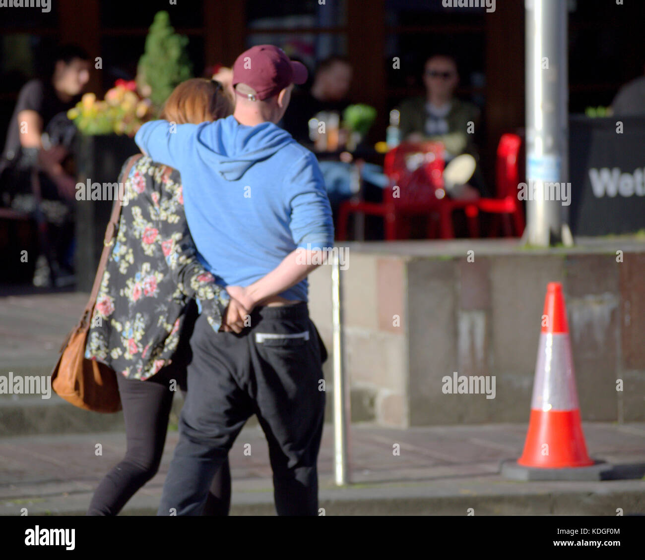 Jeune couple à la mode dans les bras de soleil balade à Glasgow en Écosse, le rue avec cône de trafic vu de derrière Banque D'Images