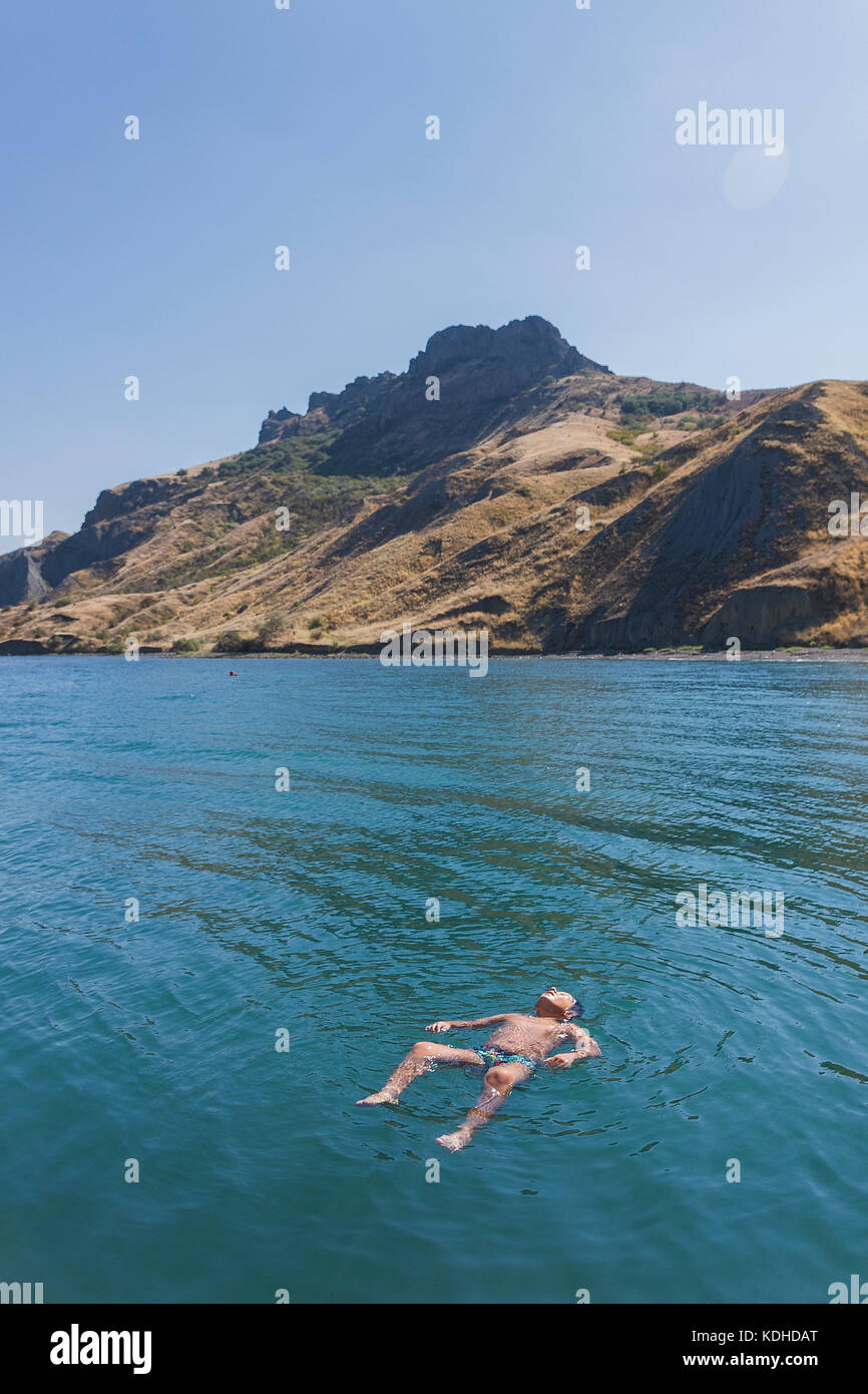 Petit garçon se repose en flottant sur l'eau de mer sur le dos Banque D'Images