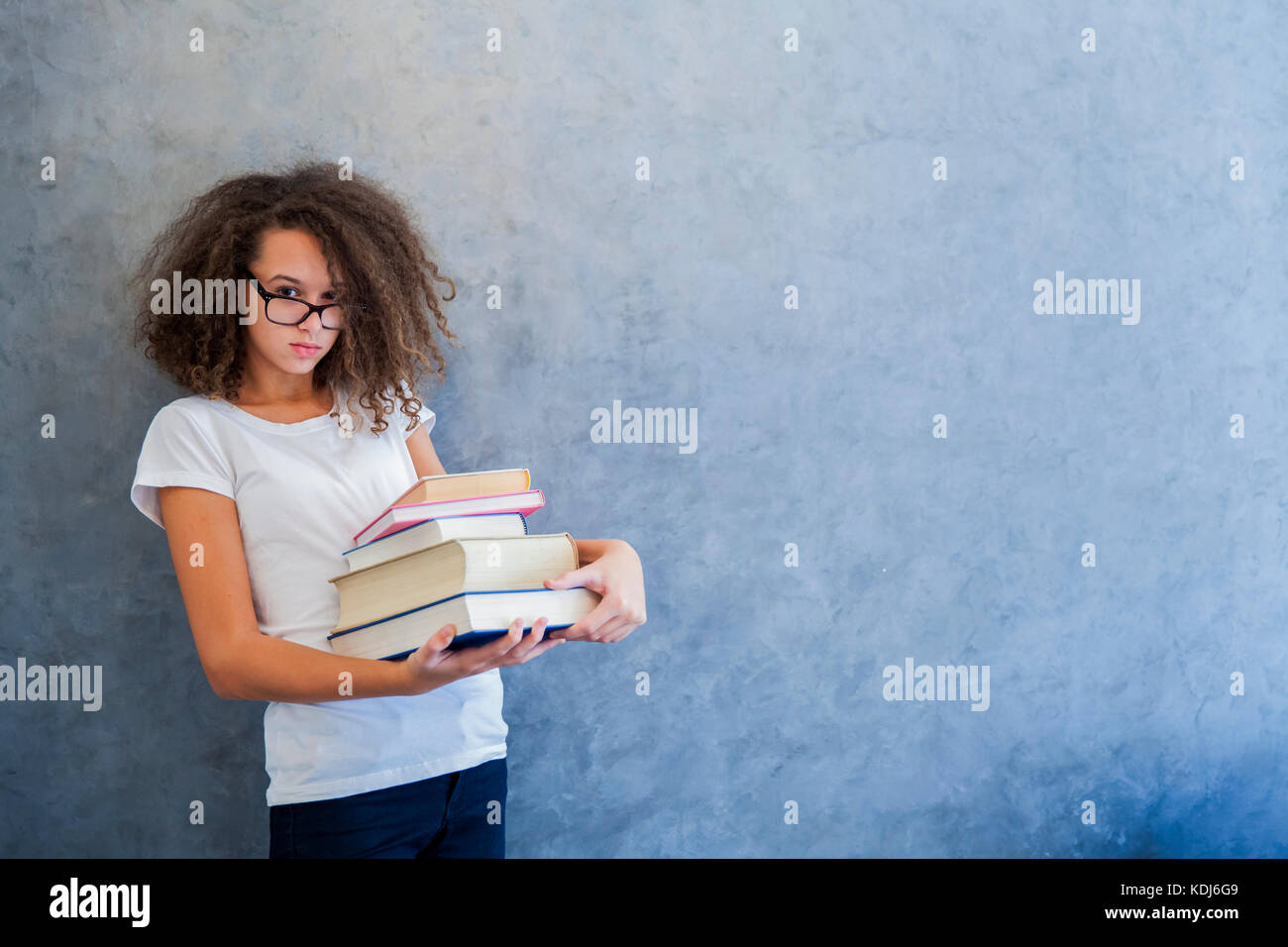 Portrait of teenage girl avec des lunettes se dresse à côté du mur et détient plusieurs livres Banque D'Images