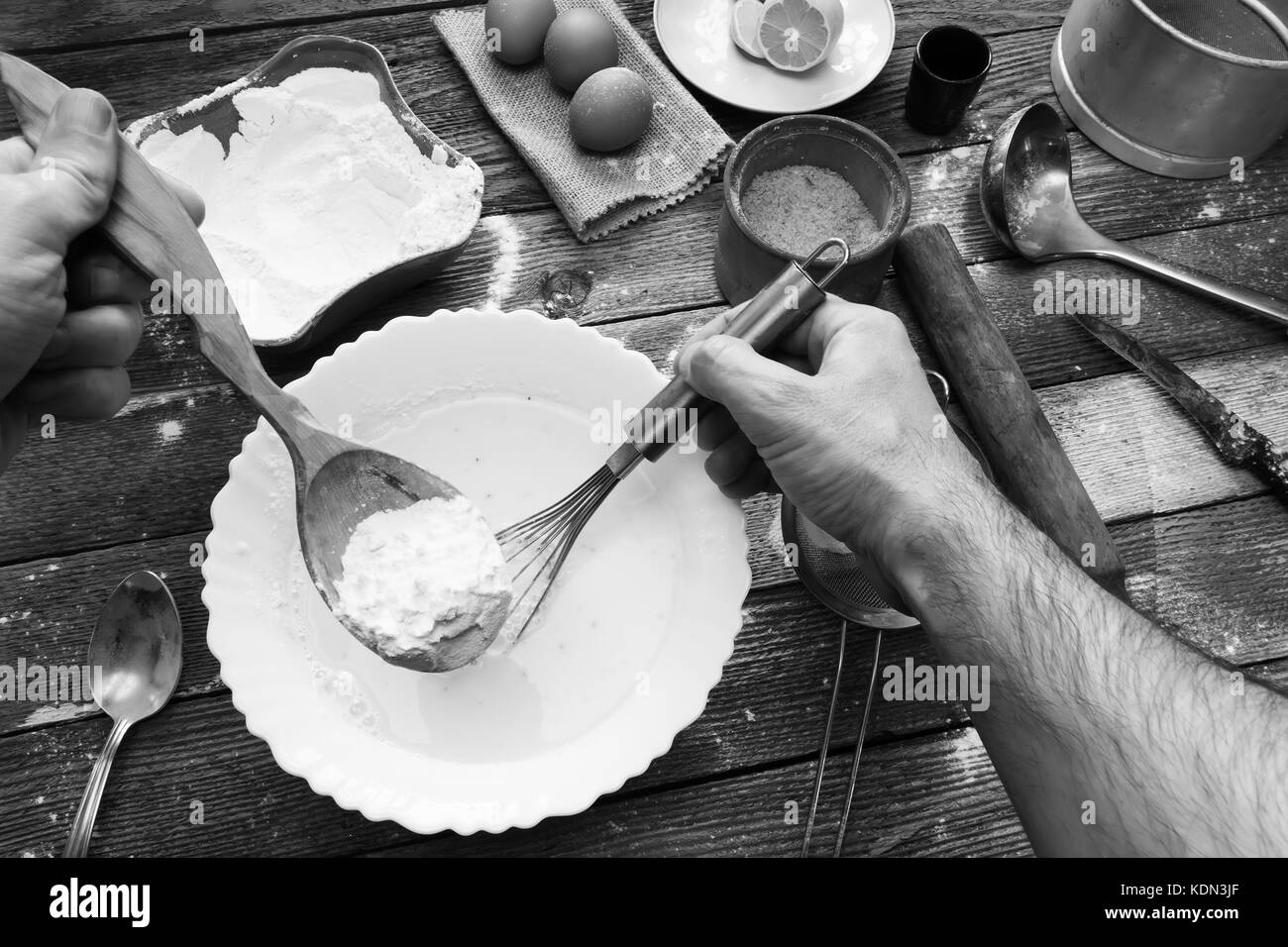 L'homme pétrir la pâte avec un fouet. La farine de blé, oeufs, pâte, un  citron et des ustensiles de cuisine sur la table en bois. Préparation de la  pâte dans un cadre