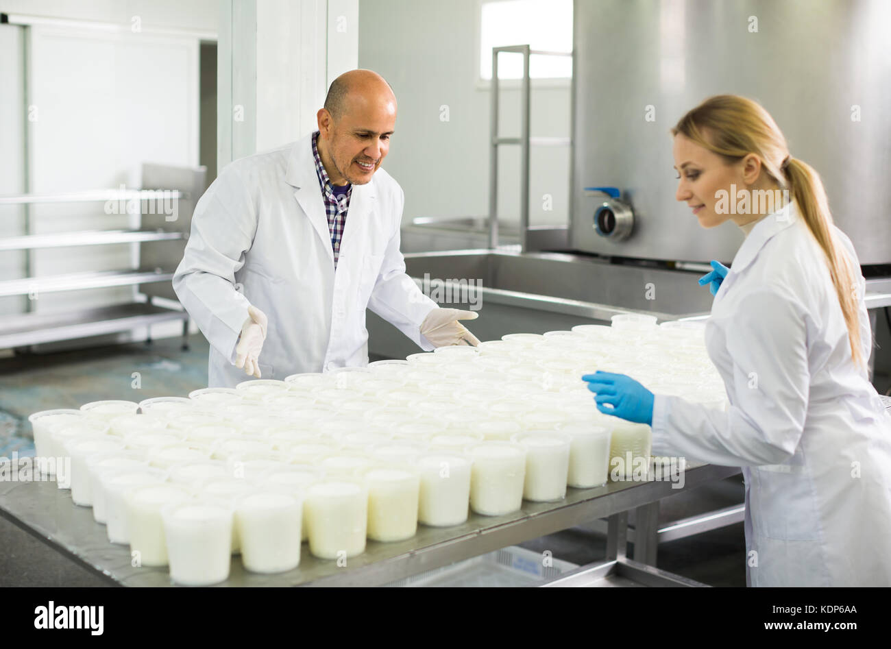 Deux travailleurs séropositifs en blouse blanche qui travaillent à la production du fromage cottage sur l'usine laitière. L'accent sur l'homme Banque D'Images