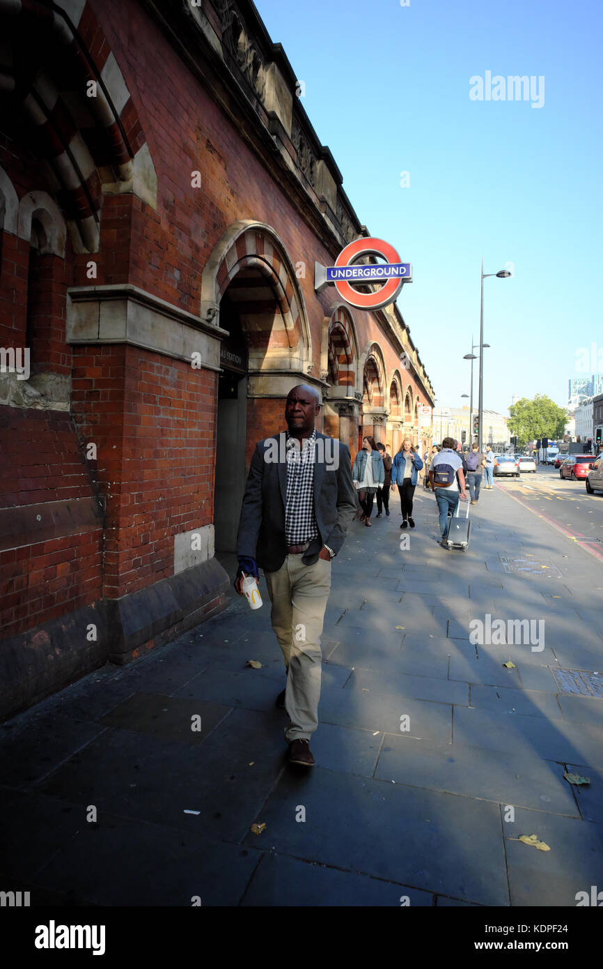 Caraïbes Afrique de l'homme avec un verre à la main, signe de métro marche passé St Pancras Islington, Londres, Angleterre Banque D'Images