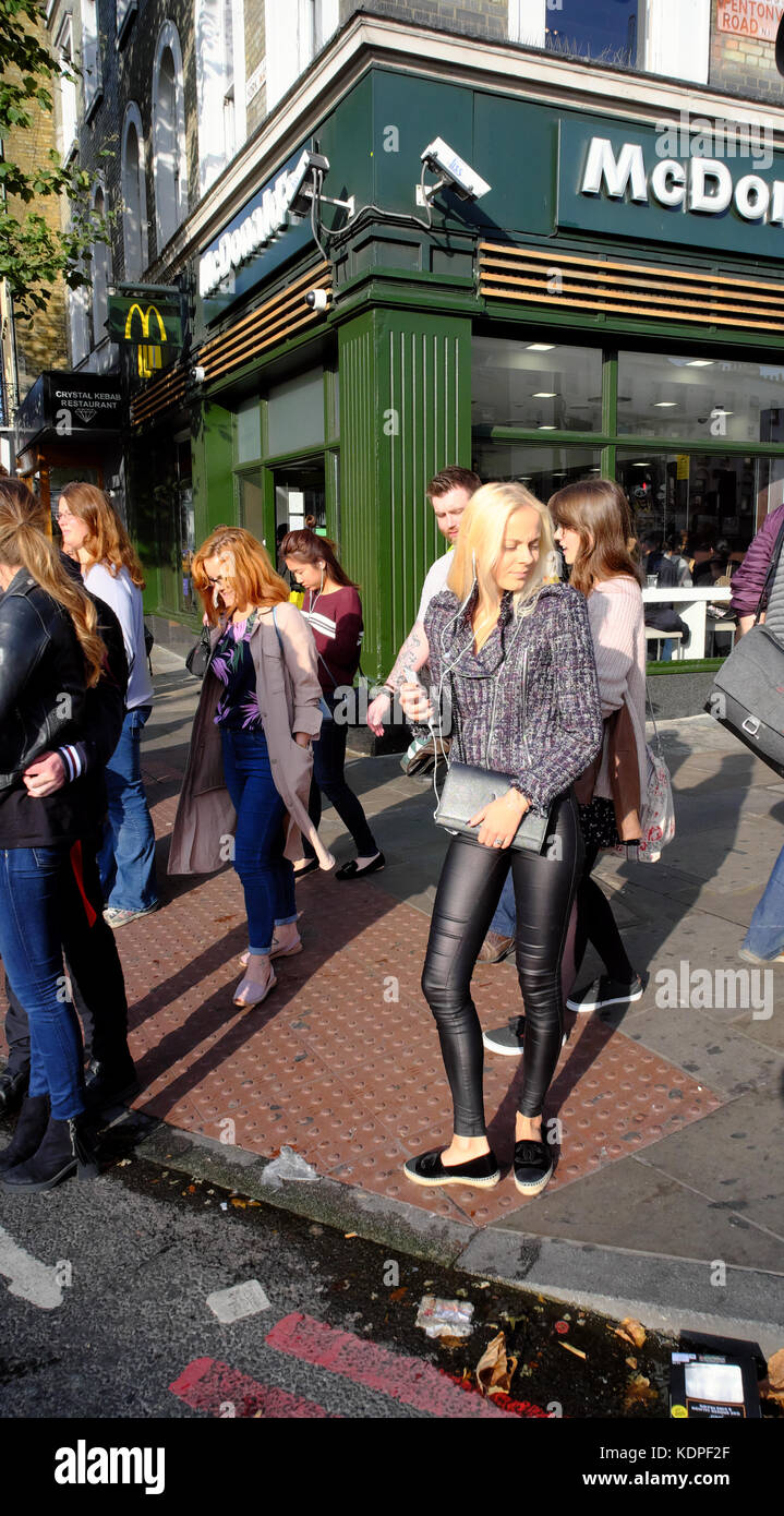 Blond woman wearing Jeans en cuir serré debout sur freiner alors que les gens à pied adoptée par Mcdonald's, Kings Cross, Islington, Londres, Angleterre Banque D'Images