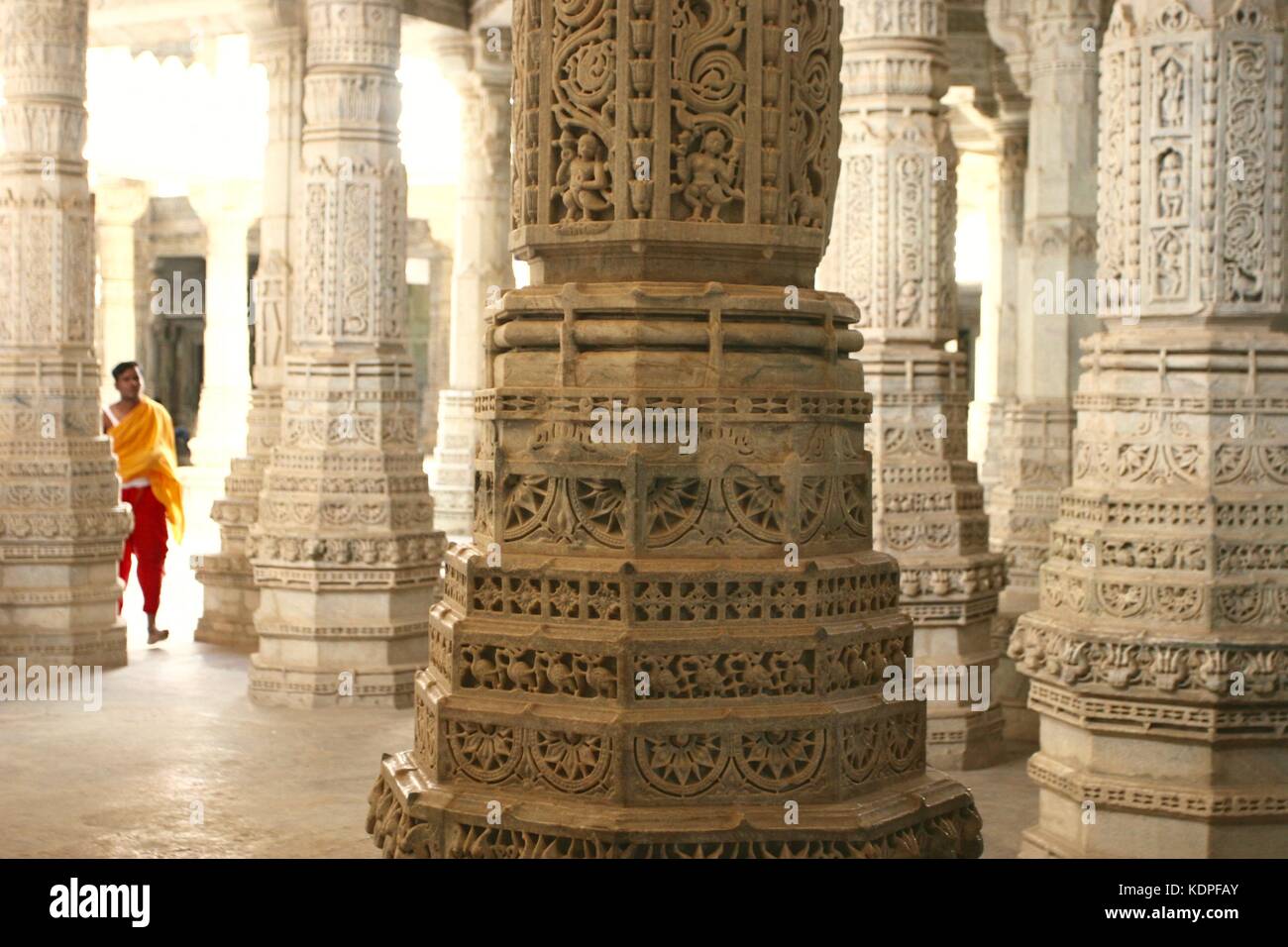 Un moine dans une robe orange marche parmi des colonnes dans le temple Ranakpur Jain au Rajasthan, Inde Banque D'Images