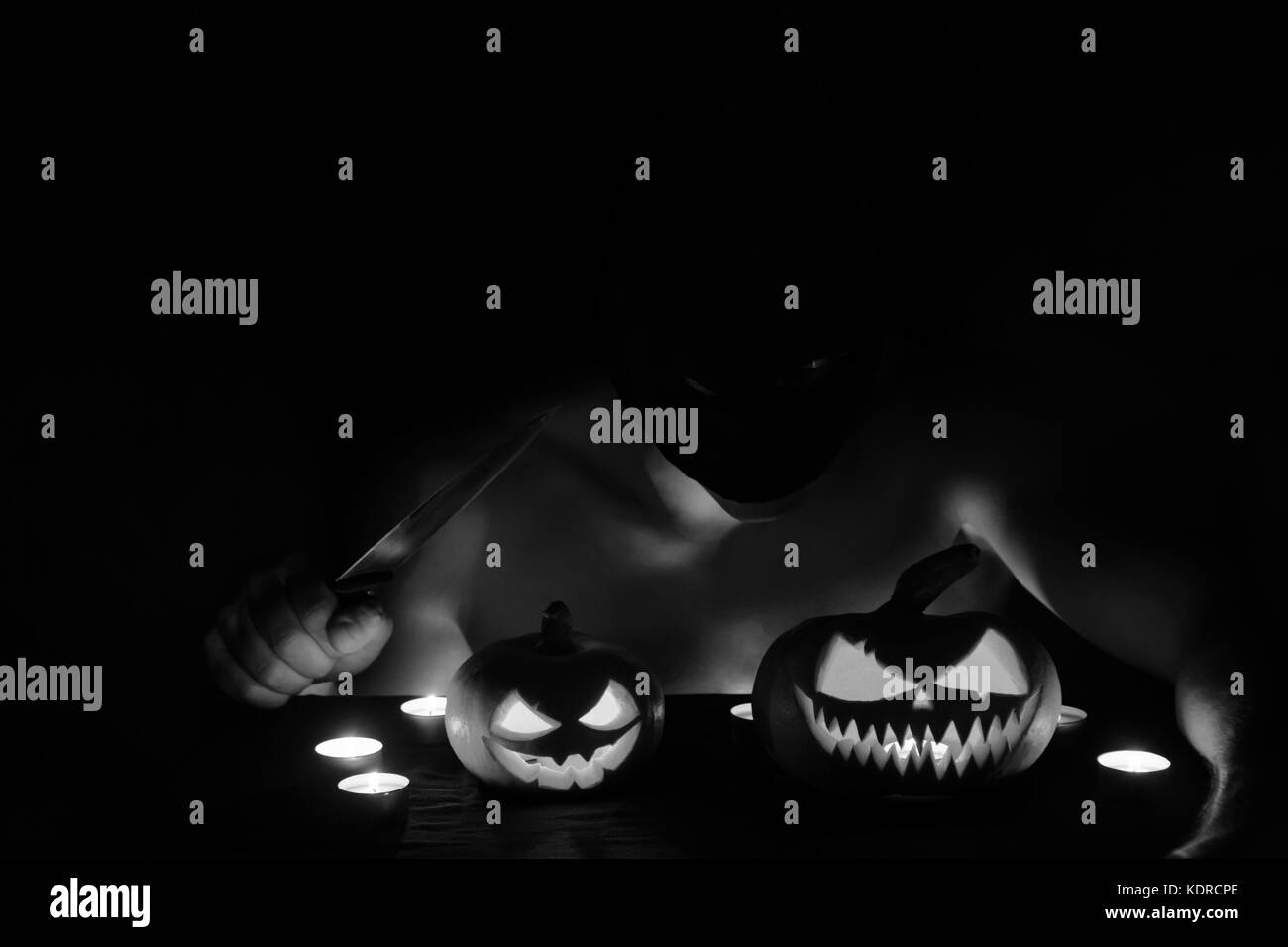 Un gars déguisé en un maniaque est assis avec un couteau, et il y en a deux de citrouille sur la table. halloween art design. Banque D'Images