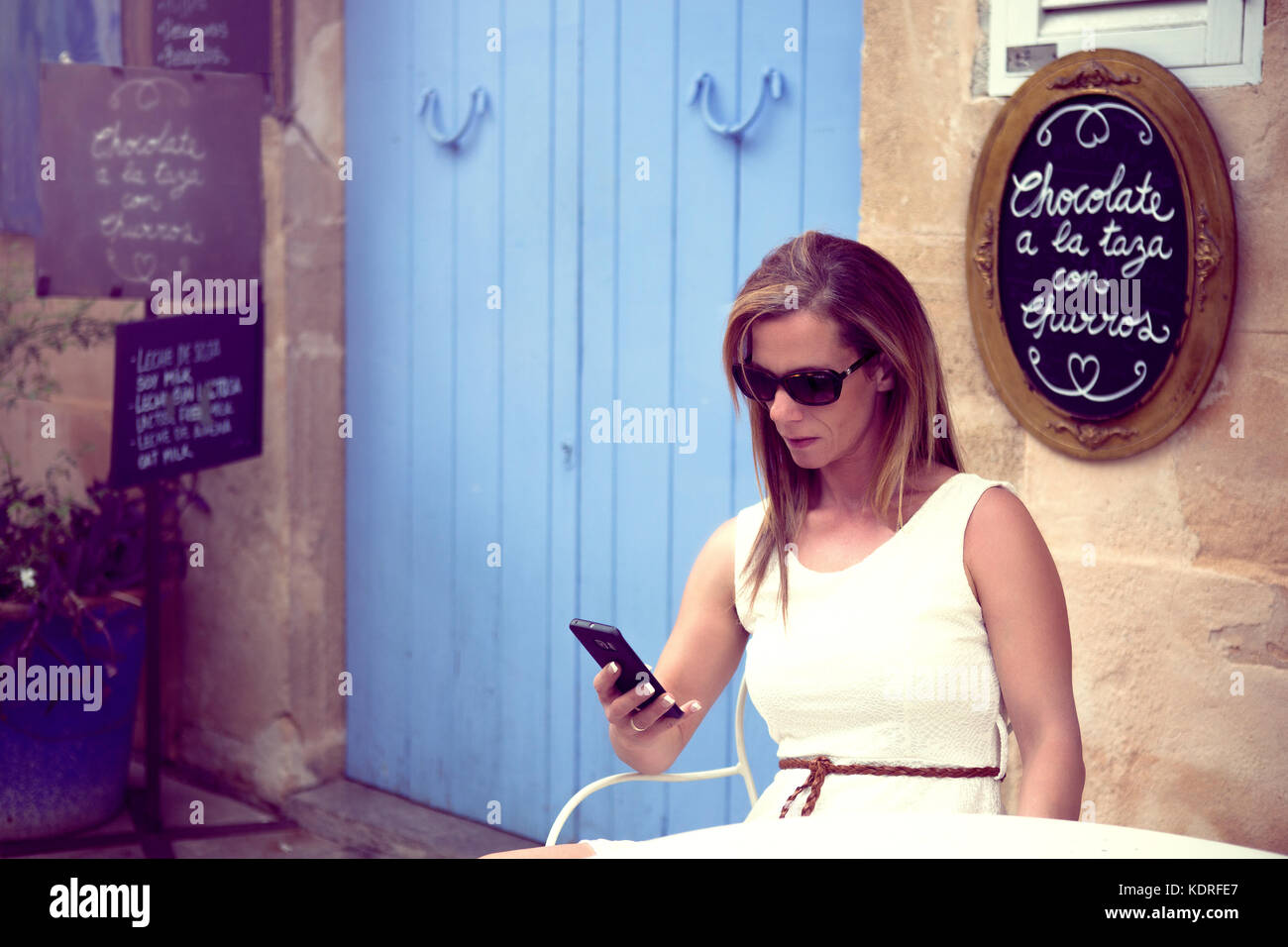 L'Europe, Espagne, Baléares, Mallorca, centre historique d'Arta - une jeune femme assise dans un café à Arta et contrôler son téléphone / tablett Banque D'Images