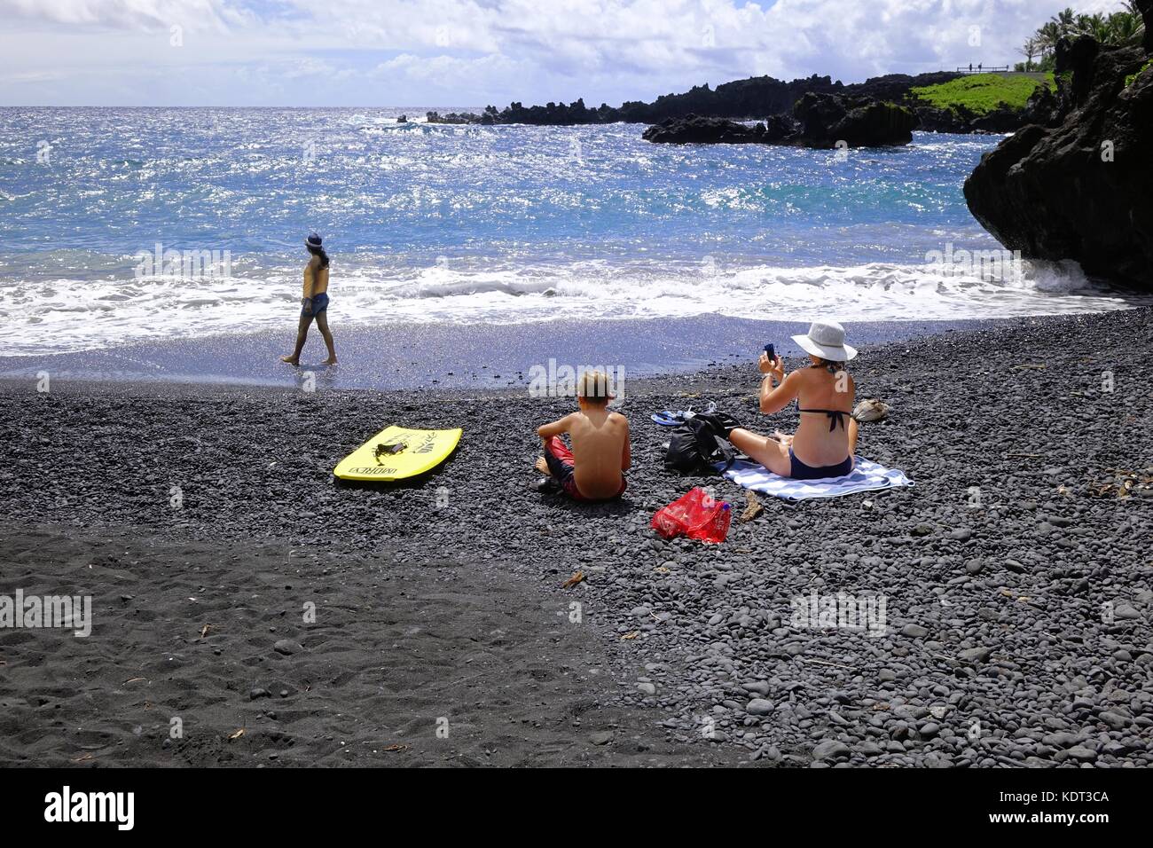 Femme et enfant assis sur la plage de sable noir, Waianapanapa State Park, sur la route de Hana, Maui, Hawaii Banque D'Images