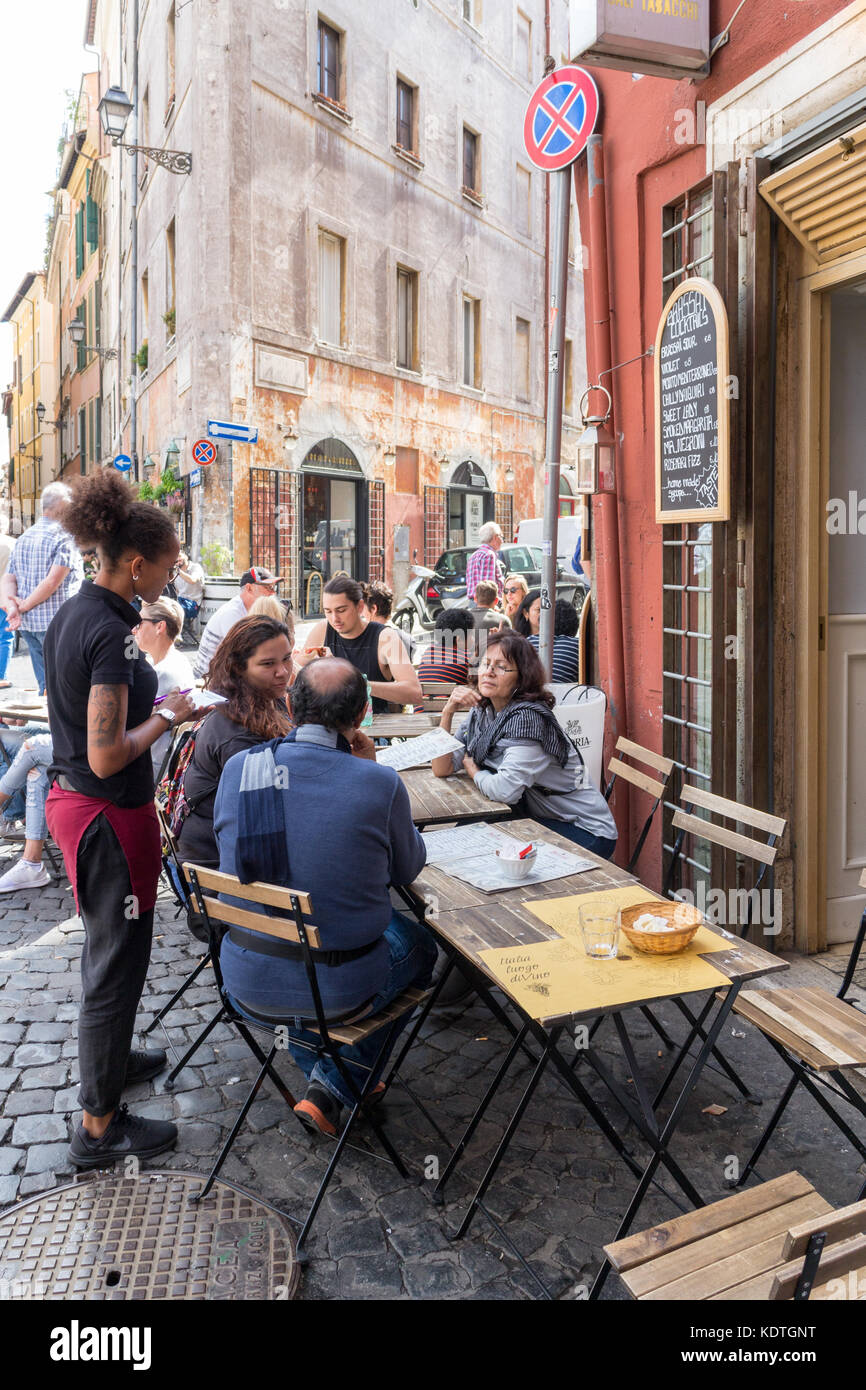 Les gens assis à des tables de restaurant dans une rue de Rome, Italie Banque D'Images