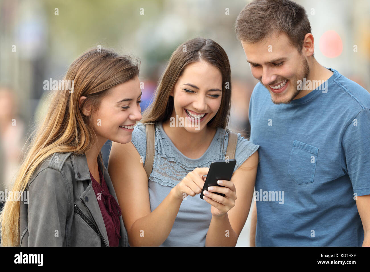 Trois amis heureux smart phone contrôle permanent du contenu à l'extérieur dans la rue Banque D'Images