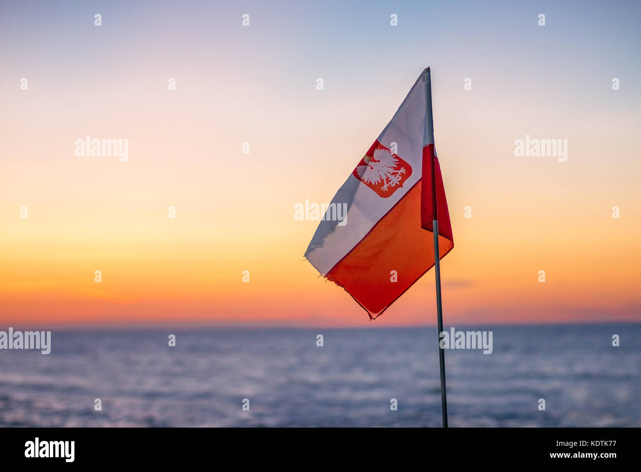 Le rouge et le blanc du drapeau national polonais avec l'emblème de l'aigle palpitations dans le vent sur une plage au coucher du soleil Banque D'Images