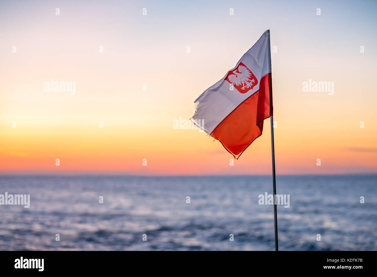 Le rouge et le blanc du drapeau national polonais avec l'emblème de l'aigle  palpitations dans le vent sur une plage au coucher du soleil Photo Stock -  Alamy