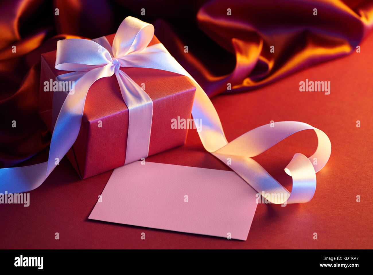 Boîte-cadeau avec ruban en forme de coeur sur fond rouge Banque D'Images