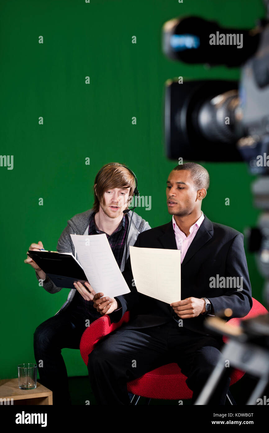 Le gestionnaire d'étage passe en revue les scripts avec un présentateur de télévision dans un studio à écran vert. Caméra TV floue au premier plan. Un peu de flou de mouvement s'active Banque D'Images