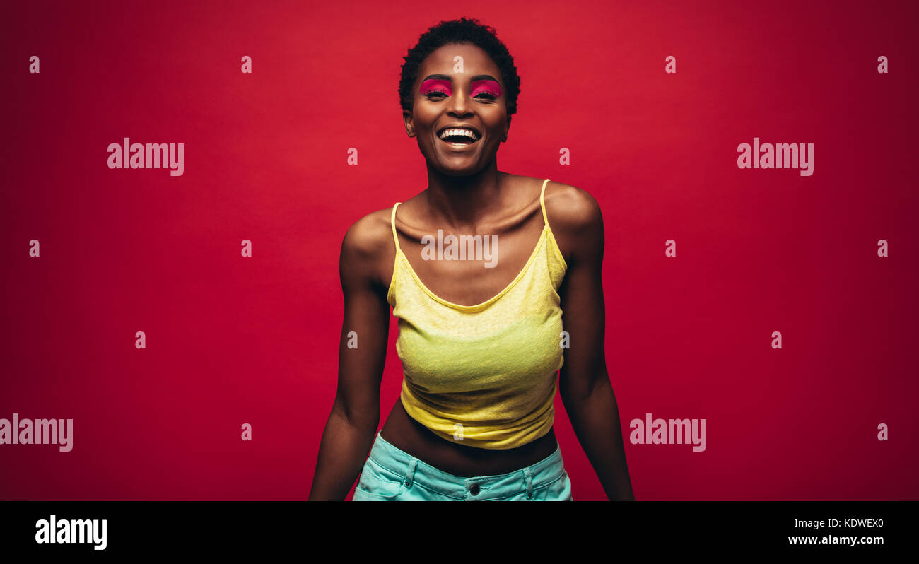 Belle jeune femme africaine sur fond rouge. Cheerful fashion model avec maquillage colorés en studio. Banque D'Images