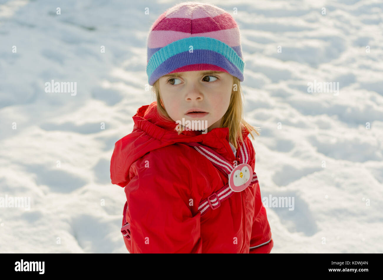 Jolie petite fille d'âge préscolaire en hiver neige scène portant des habits rouges et stripy woolly hat pendant les vacances Banque D'Images