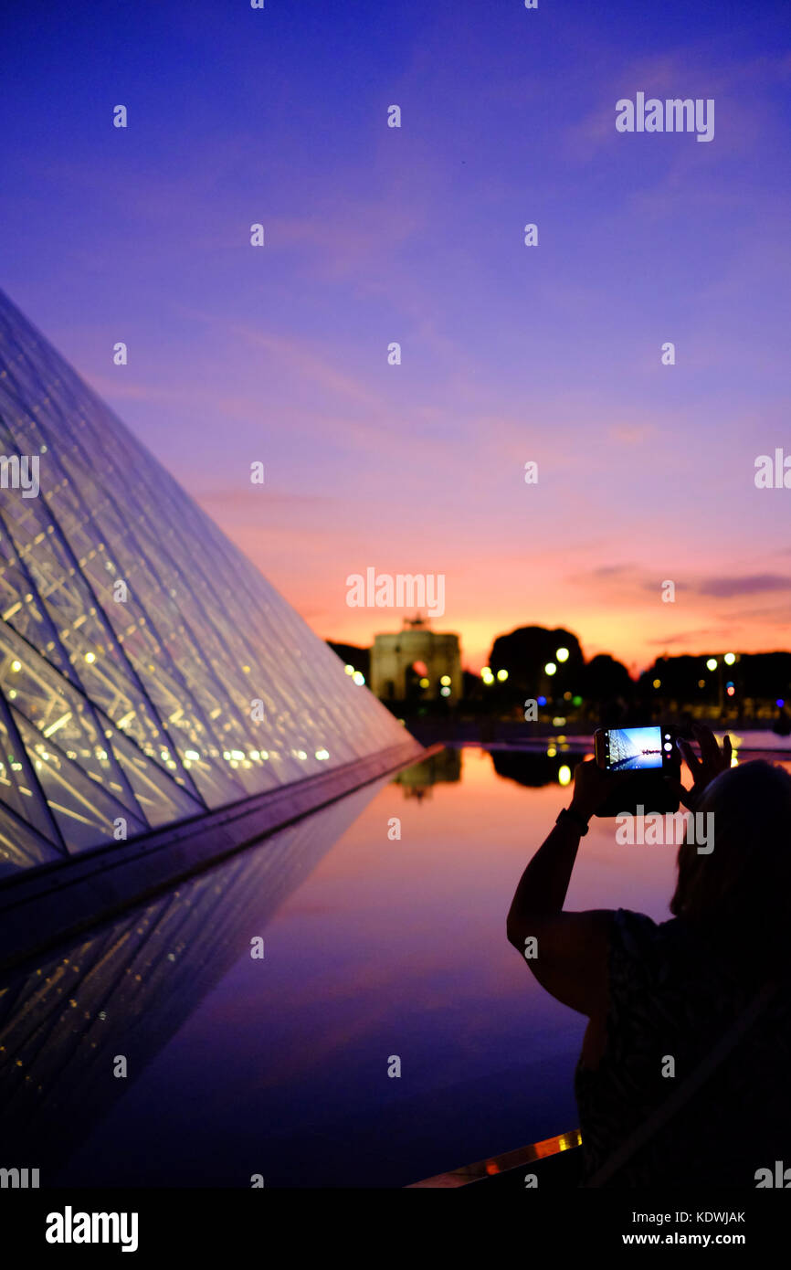 Une touriste prend une photo du Louvre nuit à Paris, à l'aide de son smartphone Banque D'Images