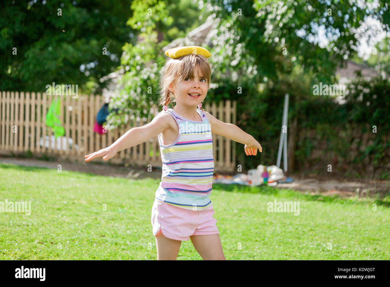 Jolie petite fille d'âge élémentaire sur l'équilibrage de la journée des sports de sac d'haricot jaune sur la tête. happy fun concept retour à l'école. Banque D'Images