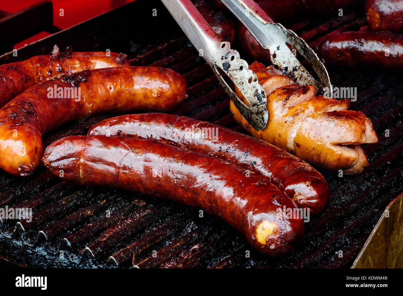 Saucisses bratwurst sur plaque de fer en fonte. metal pinces. Banque D'Images