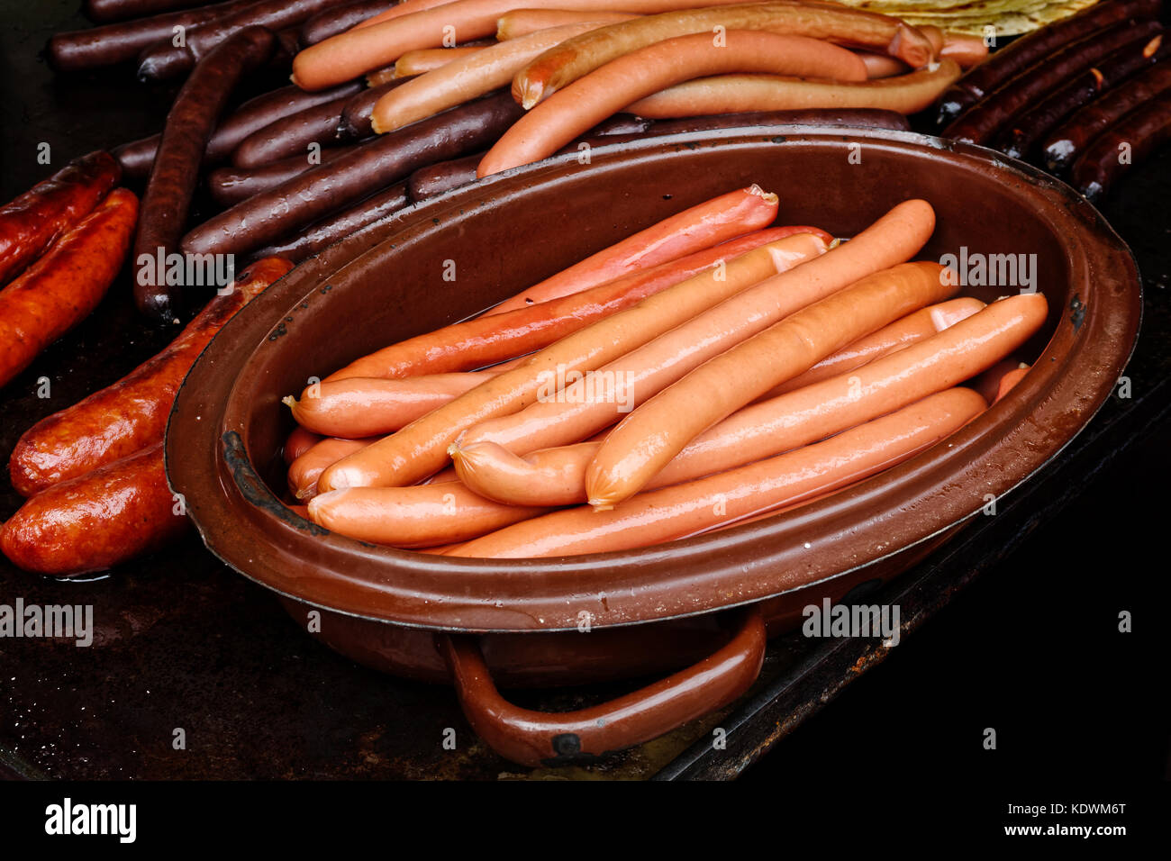 Saucisses wiener bouilli en chaudron à côté de saucisses grillées sur le gril en fonte. Banque D'Images