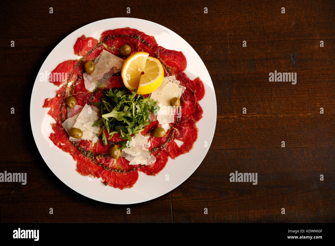 L'italien le carpaccio de boeuf avec des copeaux de parmesan et roquette isolé sur table brun foncé à partir de ci-dessus. Banque D'Images