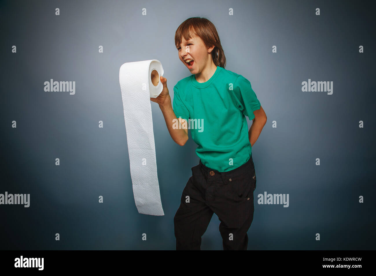 L'apparence de l'adolescent garçon cheveux brun dans une chemise tenant un papier de toilette sur un fond gris, le rire de traitement croisé Banque D'Images