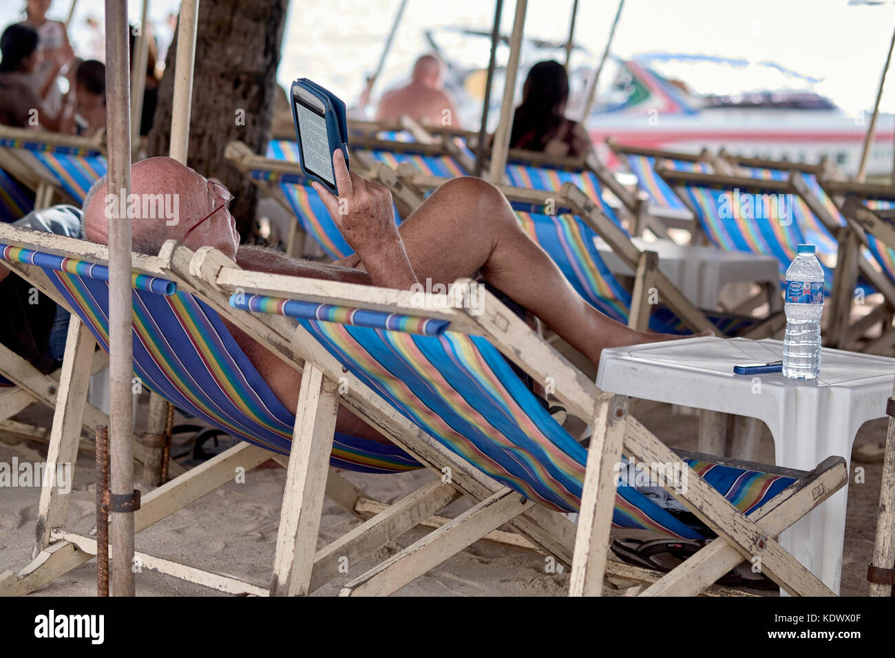 La lecture de l'homme e Kindle livre tout en vous relaxant sur la plage. Pattaya Thaïlande Asie du sud-est Banque D'Images