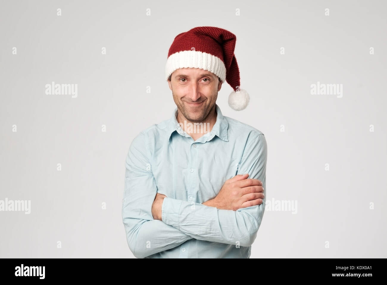 Relaxed mature man wearing santa claus hat standing avec mains croisées sur fond blanc. Banque D'Images