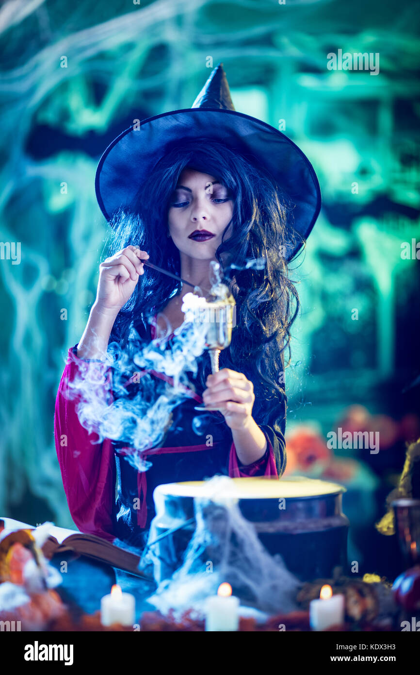 Jeune sorcière avec visage sérieusement en environs et fumé fond vert est titulaire d'un gobelet avec potion magique. Banque D'Images