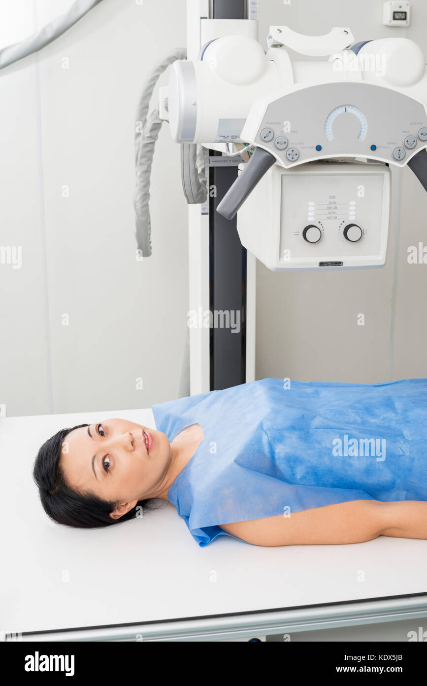 Portrait of mature female patient in vêtements de protection bleu couché sous x-ray machine en salle d'examen Banque D'Images