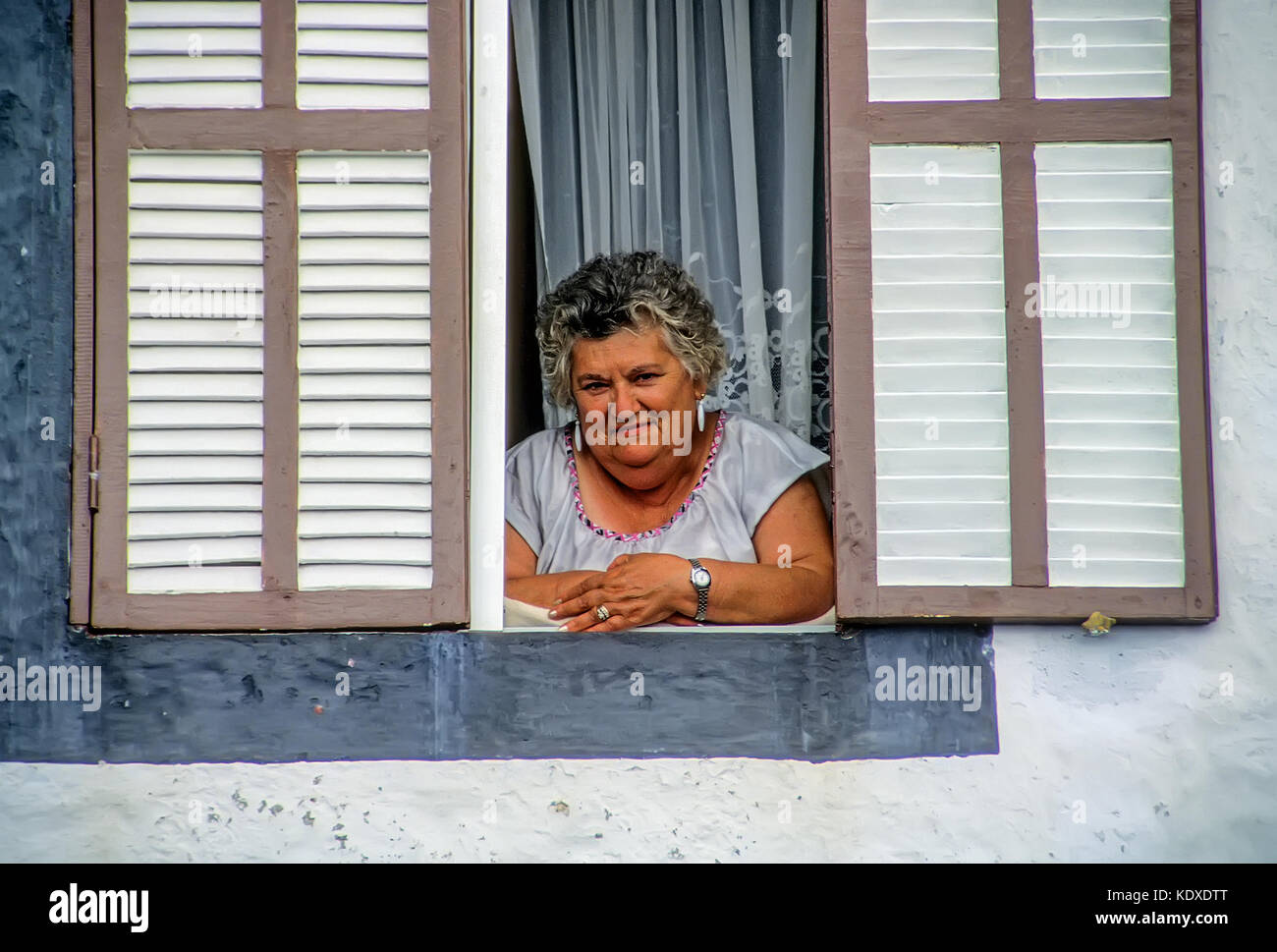 Portrait d'une femme portugaise des matronly sereinement regarder comme elle se penche à sa fenêtre d'accueil sur l'île de Pico, Açores Banque D'Images