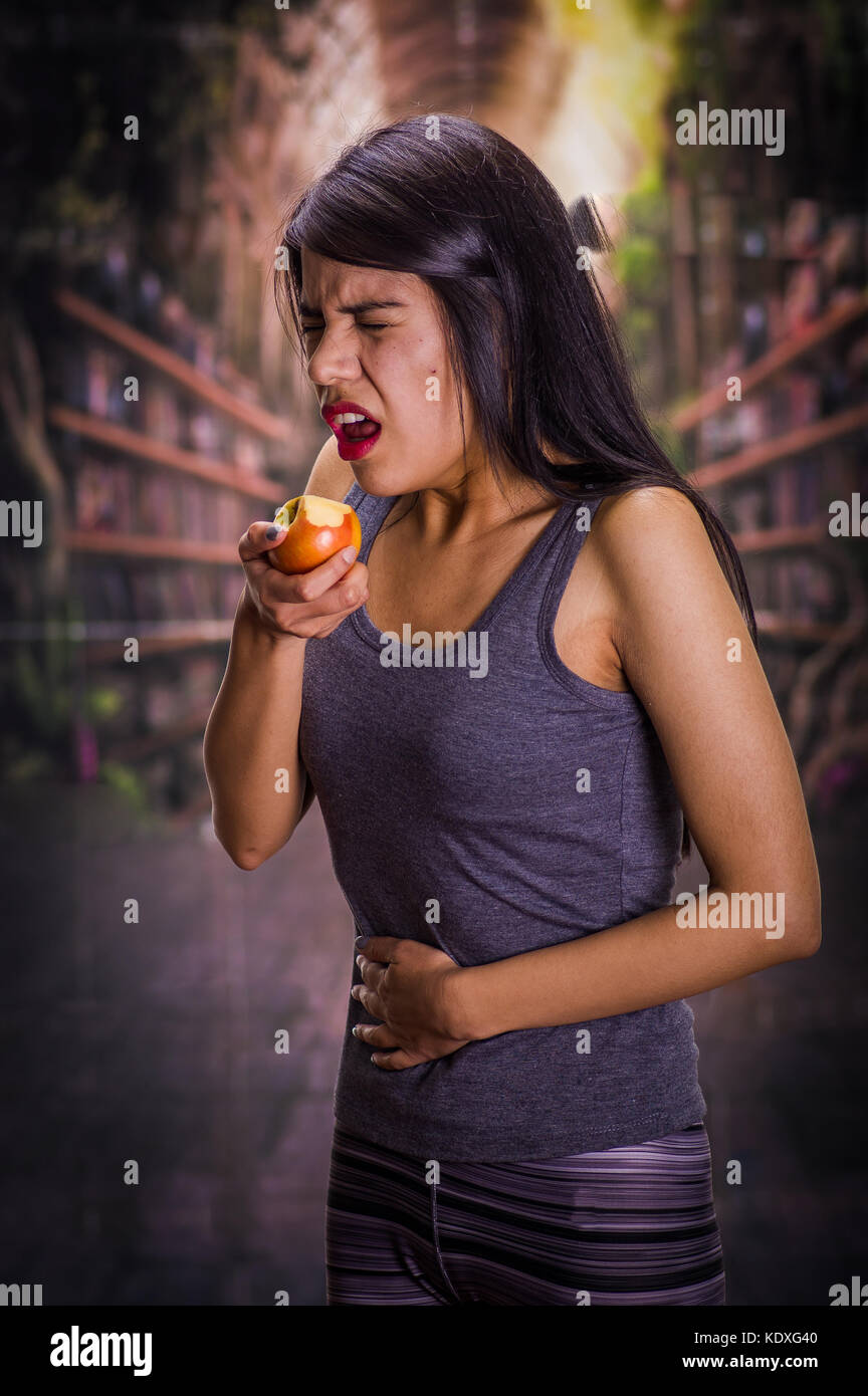 Belle jeune fille solitaire et souffrant d'anorexie, de la souffrance la douleur dans son estomac alors qu'elle mange une pomme, dans un arrière-plan flou Banque D'Images