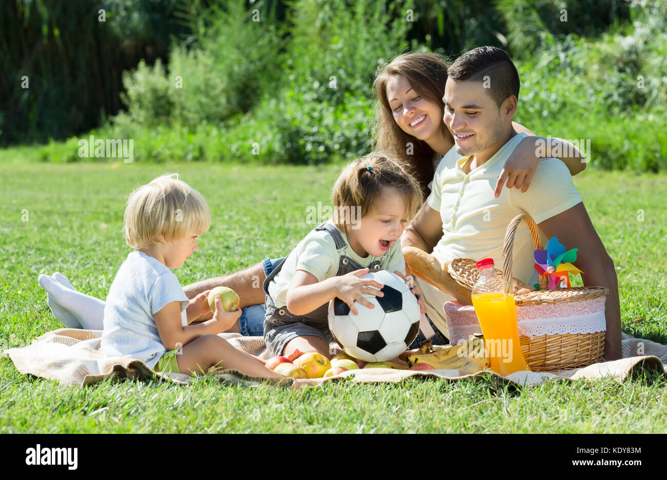 Heureux jeune famille de quatre having picnic à meadow. se concentrer sur l'homme Banque D'Images