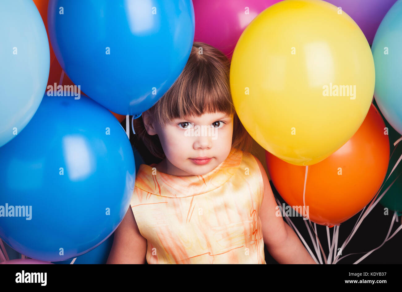 Portrait of caucasian blonde petite fille aux ballons colorés sur fond noir Banque D'Images