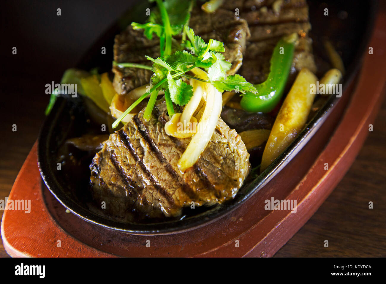 Pavé de boeuf grillé servi avec une poêlée de légumes et surmontées de coriandre. Le plat est un exemple de la cuisine fusion. Banque D'Images