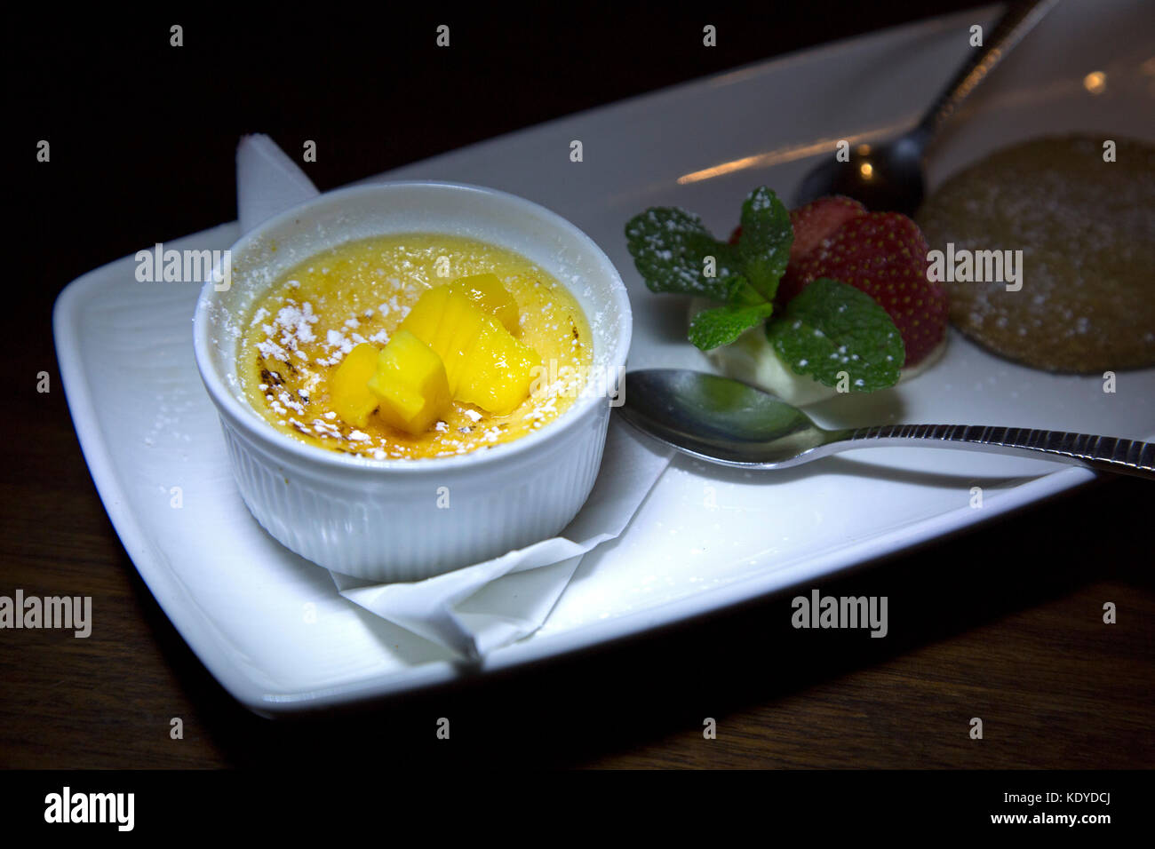 Crème brûlée à la mangue servi. Le dessert est présenté avec de la crème et de tranches de fraise et d'un biscuit sablé lavande. Banque D'Images