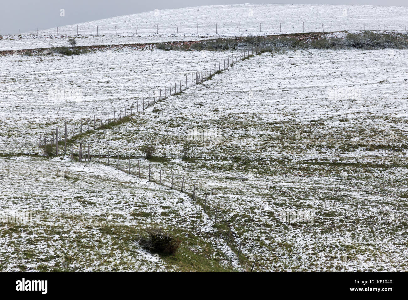 Une clôture en cours d'exécution sur une montagne, au milieu de la neige couvrant partiellement l'herbe meadows Banque D'Images