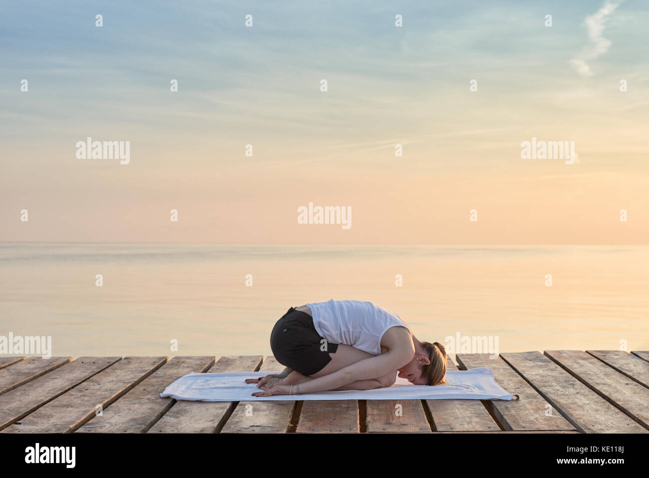 Vue arrière du jeune femme était assise sur la pratique du yoga serviette par mer au coucher du soleil Banque D'Images