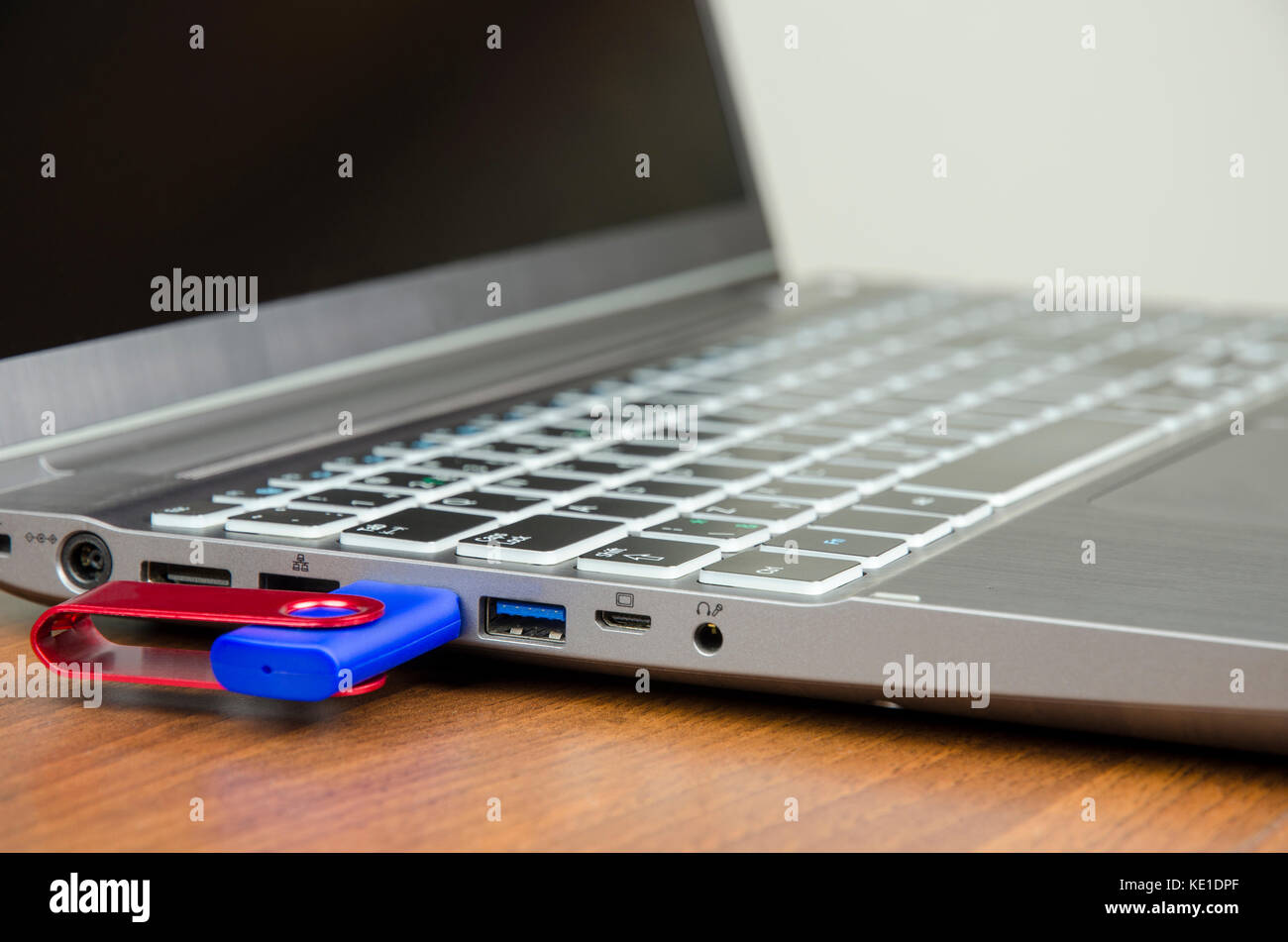 Vue rapprochée d'un ordinateur portable d'argent avec disque flash bleu attaché sur une table de bois et sur un fond blanc Banque D'Images