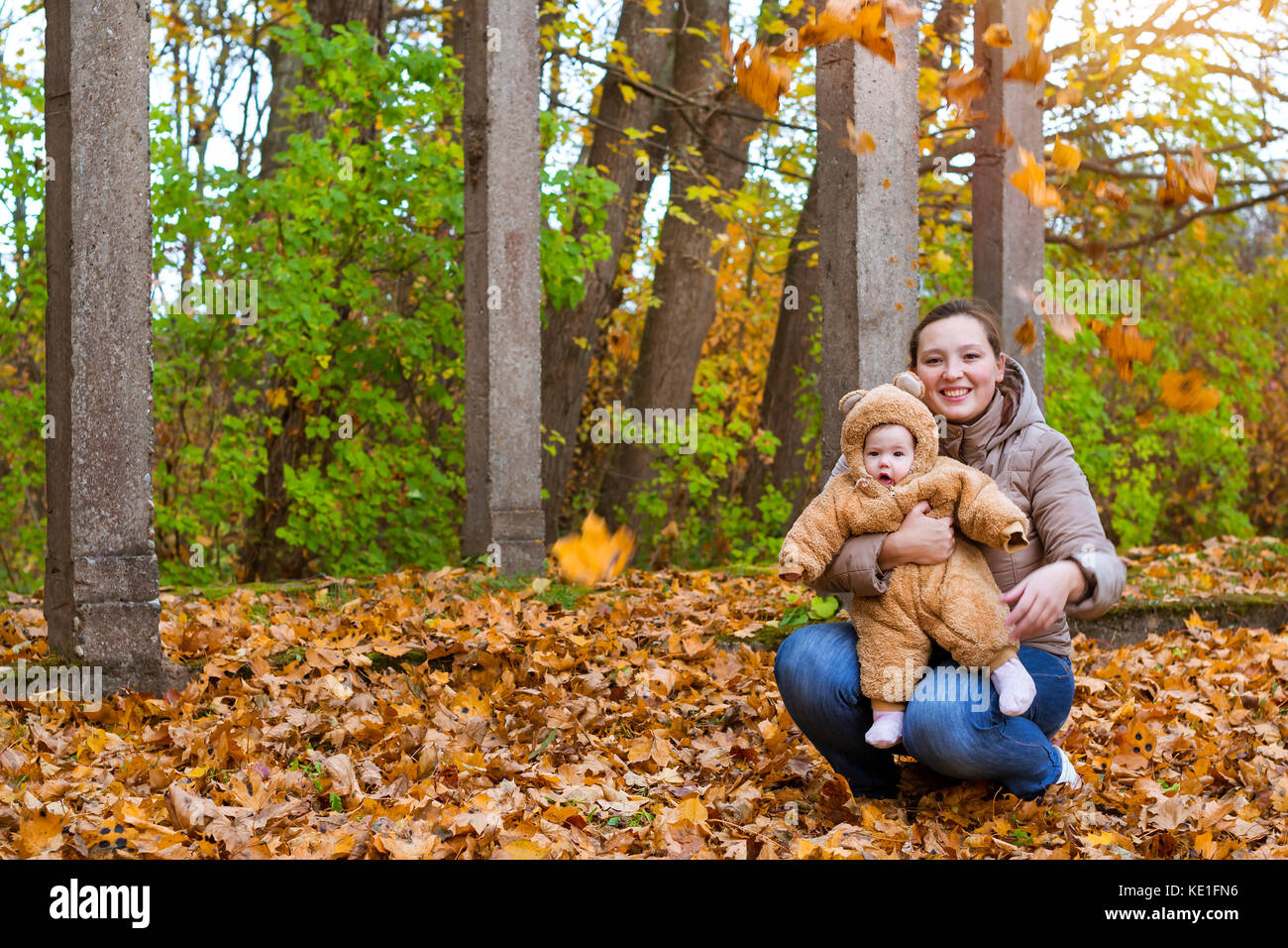 Femme avec bébé dans les bras, posant sur fond d'automne parc. enfant vêtu de teddy-bear stylisé chaud costume, s'amusant sur les bras de la mère de famille. w Banque D'Images