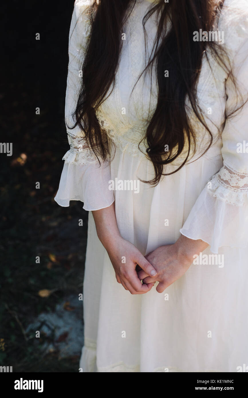 Une fille avec de longs cheveux bruns portant une robe blanche vintage avec ses mains jointes devant elle, uk Banque D'Images