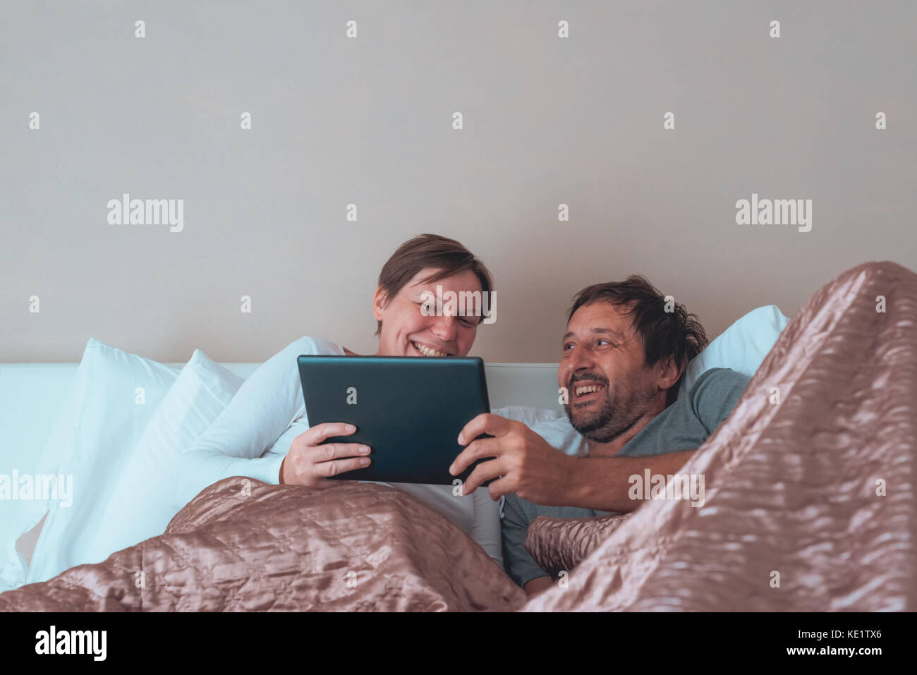Heureux couple, mari et femme dans la chambre à l'aide d'appareils électroniques personnels Banque D'Images