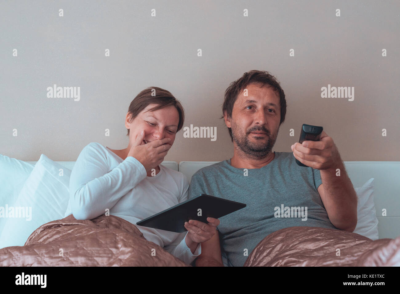 Heureux couple, mari et femme dans la chambre à l'aide d'appareils électroniques personnels Banque D'Images