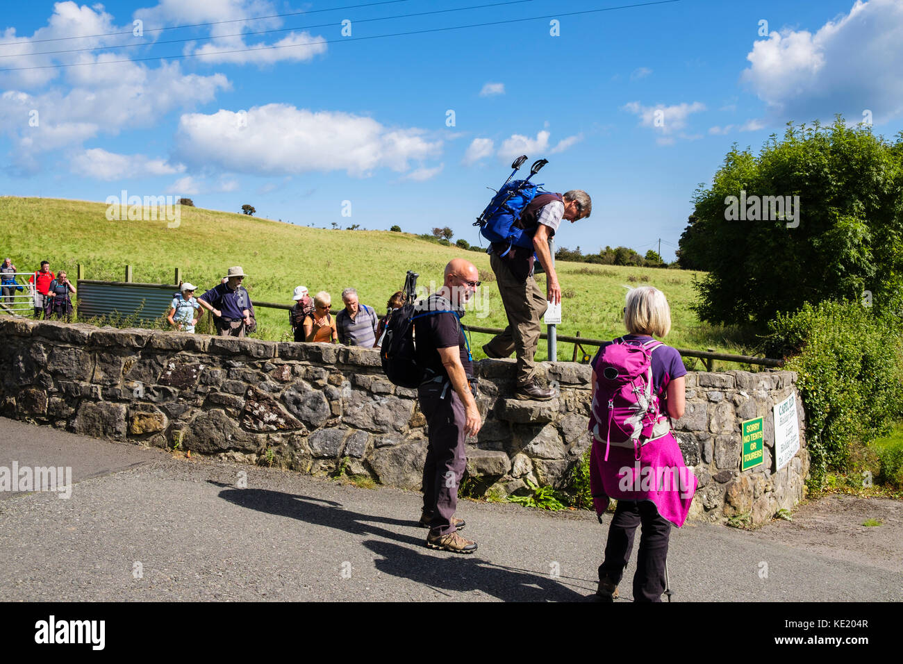 Randonneurs grimpant sur un mur de pierre stile sur un pays de marche. Lligwy, Isle of Anglesey, au nord du Pays de Galles, Royaume-Uni, Angleterre Banque D'Images