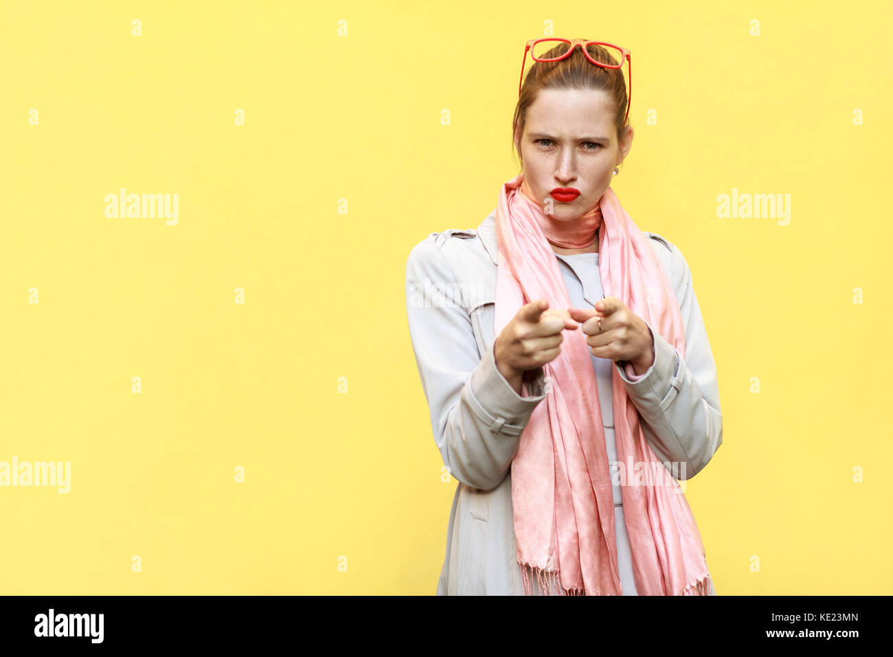 La gravité de la femme, portant manteau, ayant l'air colère, face à l'appareil photo. isolated tourné sur mur jaune Banque D'Images