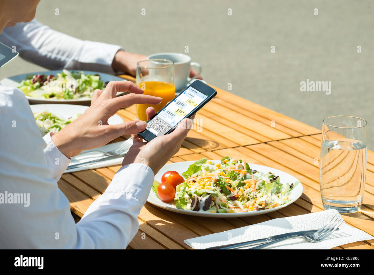 Personne chat sur téléphone mobile avec la nourriture et verre de jus sur la table Banque D'Images
