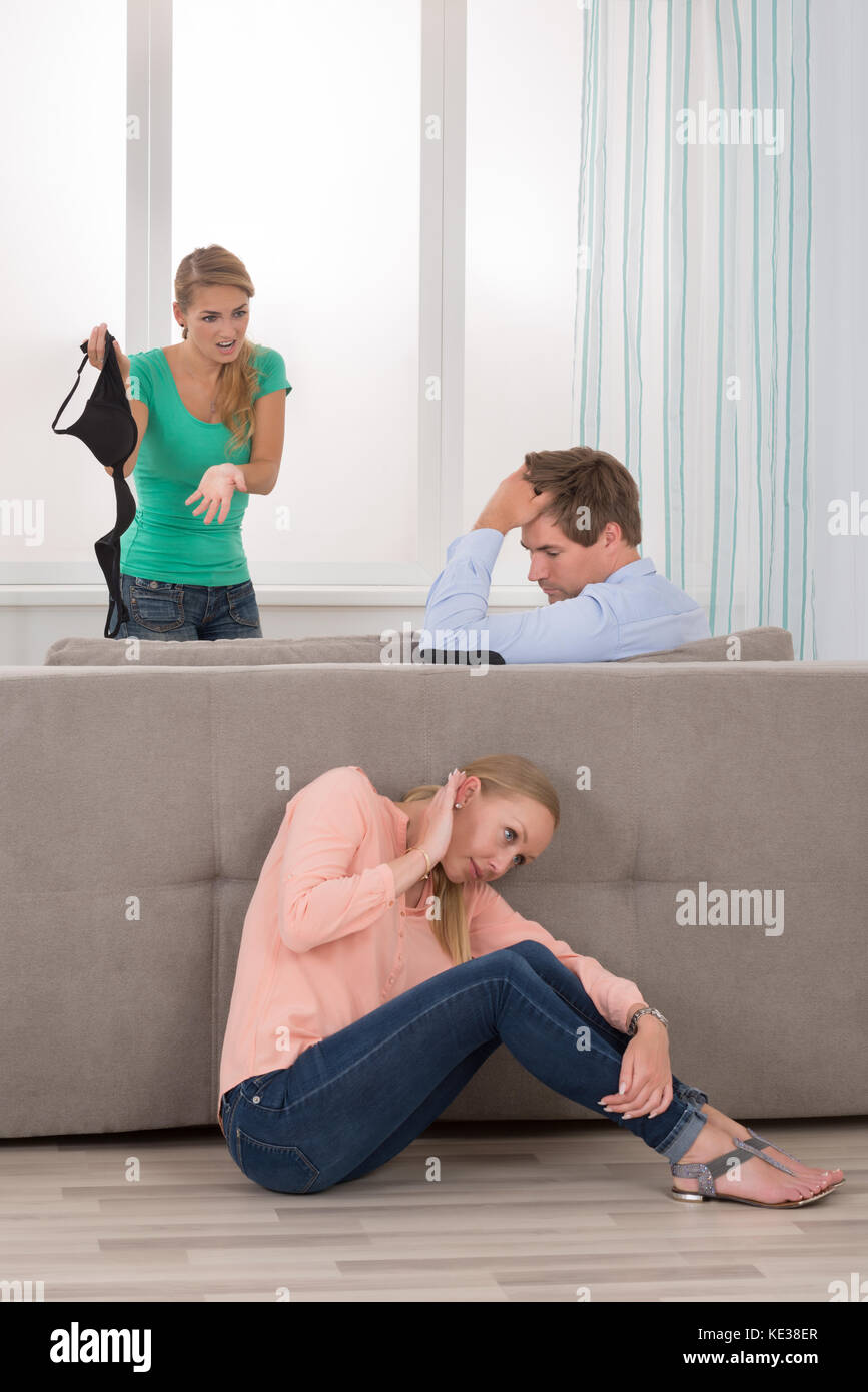 Wife Holding Bra se disputer avec son mari alors que sa petite amie se  cacher derrière un canapé Photo Stock - Alamy