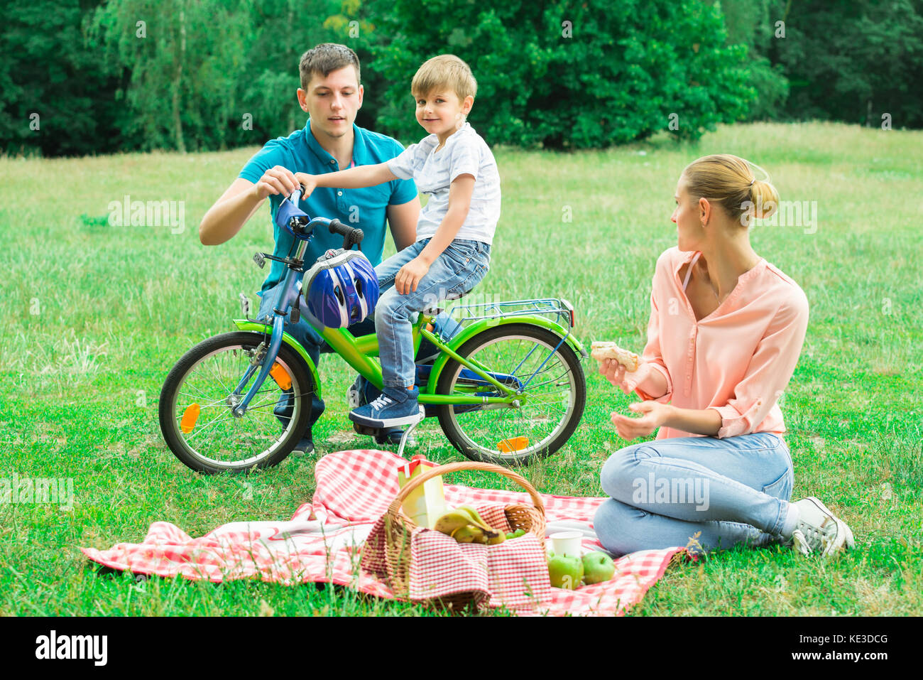Femme à la recherche d'un homme d'enseigner son fils à faire du vélo dans la région de Park Banque D'Images